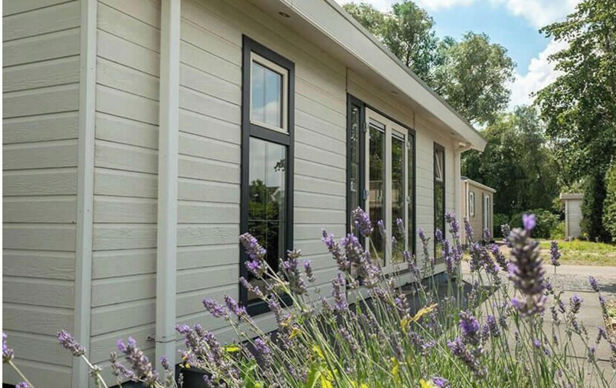Um edifício térreo com fachada clara, grandes janelas e um jardim com plantas de lavanda.