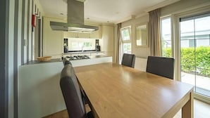 A modern kitchen with a central island, a dining area with a large table and chairs, and a view of greenery outside. - Holiday Home in Dordrecht With Terrace (Dordrecht)