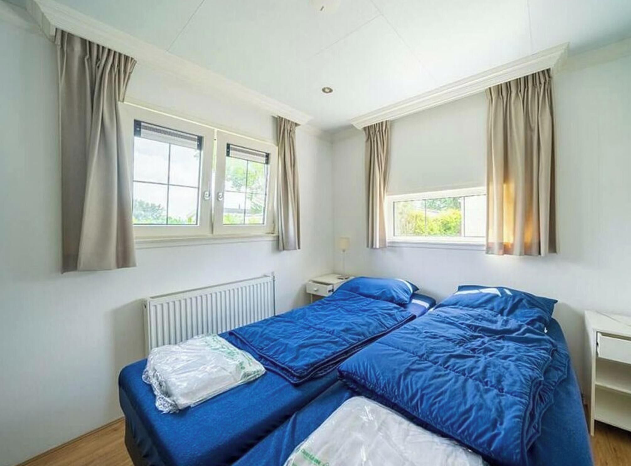 Quarto com duas camas, um radiador, uma janela e cortinas.