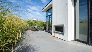 Un patio moderno al aire libre con mesa y sillas, una chimenea empotrada y vistas al cielo.