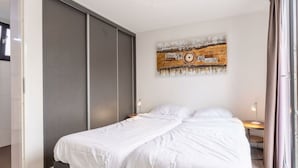 Un dormitorio con cama, armario, cuadro y mesita de noche.