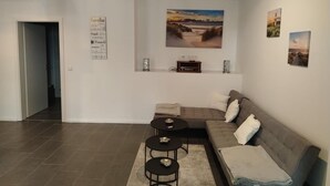 Ein Wohnzimmer mit einem Ecksofa, zwei runden Couchtischen, einem Teppich und Wandbildern.