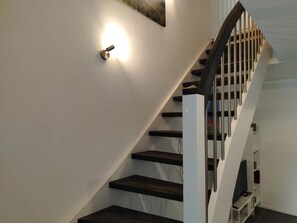 A modern staircase with a handrail, a light fixture on the wall, and a white wall.