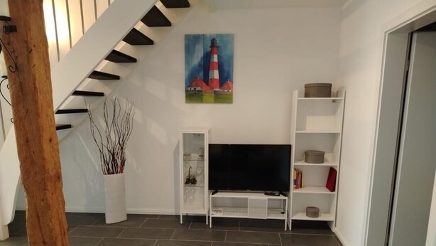Ein Wohnzimmer mit Treppe, Flachbildfernseher, weißen Regalen und einem Gemälde eines Leuchtturms.