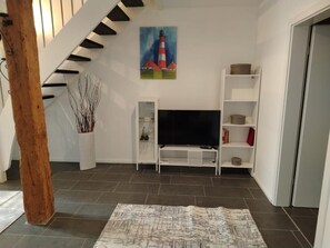 Ein Wohnzimmer mit Treppe, Flachbildfernseher, weißen Regalen und einem Gemälde eines Leuchtturms.