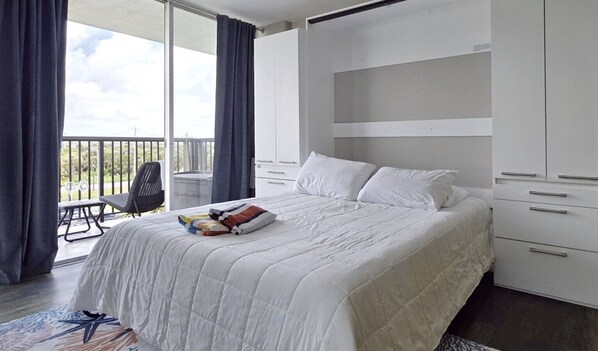 Une chambre d’hôtel avec un lit, un bureau, une chaise et un balcon avec des rideaux.