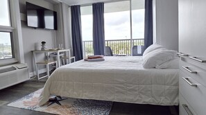 Ein Schlafzimmer mit Bett, Fernseher, Schreibtisch und einem Fenster mit Vorhängen.