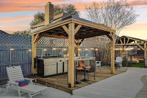 An outdoor kitchen area with a wooden pergola, a bar counter, and seating.