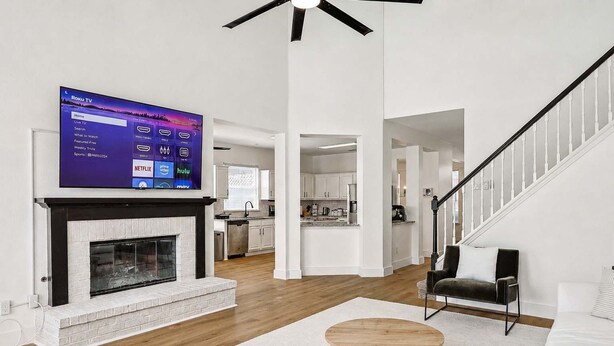 Ein modernes Wohnzimmer mit Kamin, einem montierten Fernseher, der die Roku TV-Oberfläche anzeigt, und einer Treppe, die zu einer anderen Ebene führt.