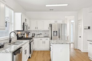 A modern kitchen with white cabinetry, granite countertops, stainless steel appliances, and a wooden floor.