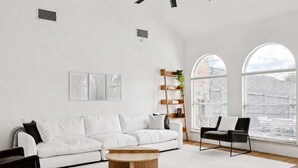 Ein modernes Wohnzimmer mit einem weißen Sofa, einem Holztisch, einem schwarzen Sessel und einem Bücherregal.