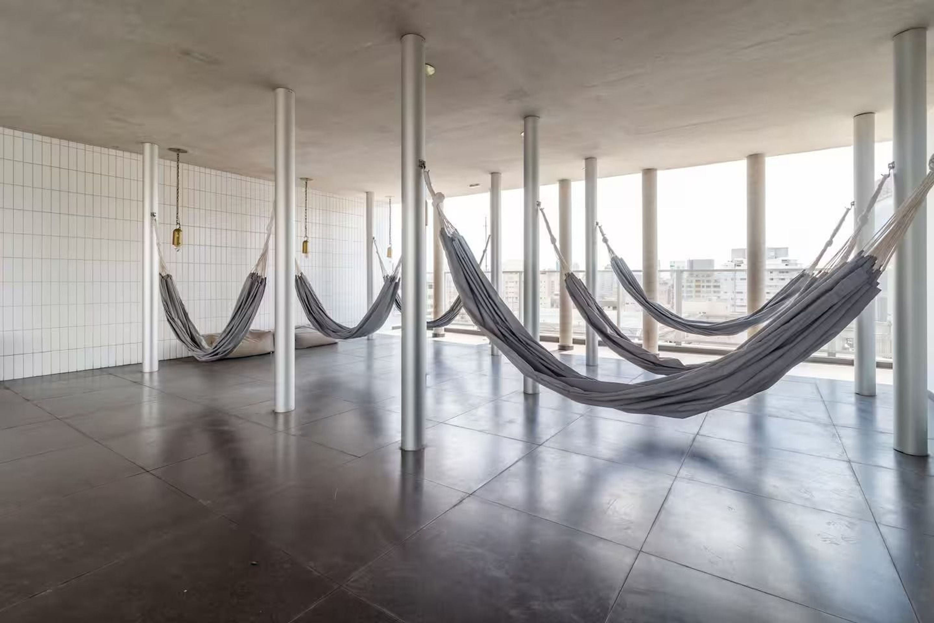 Quarto espaçoso com design moderno, com uma janela grande e uma rede pendurada entre colunas.