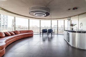 Une cuisine moderne dotée d’un îlot central aux lignes courbes, d’un coin repas avec des chaises et d’une grande fenêtre offrant une vue sur la ville.