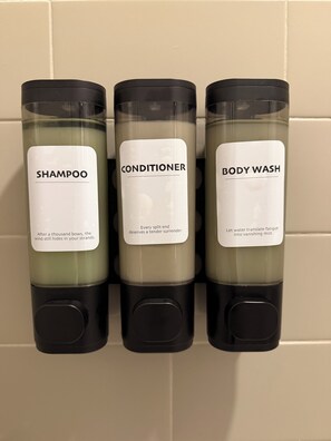 Drie flessen shampoo, conditioner en douchegel op een muur.