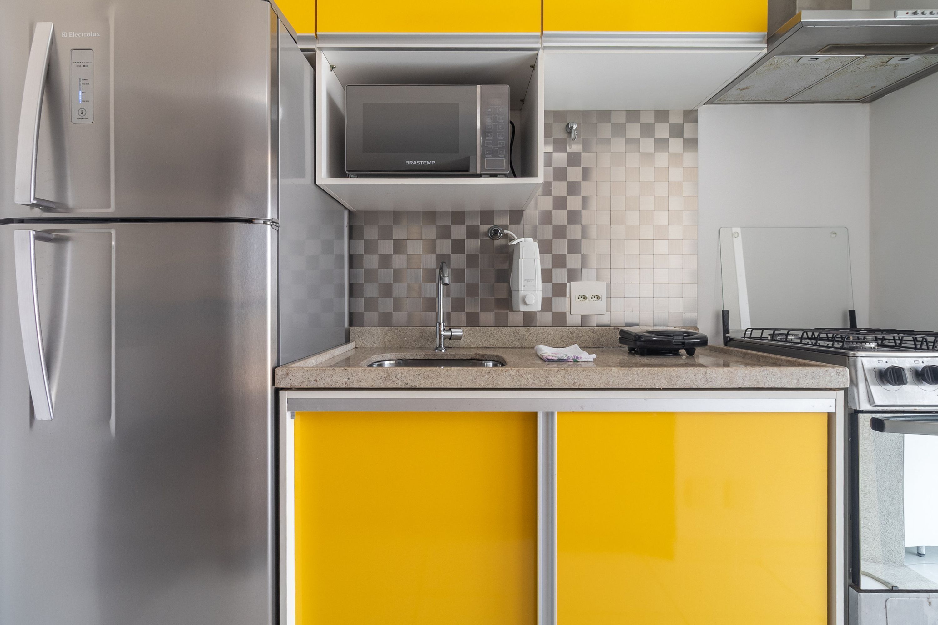 Eine Küche mit Edelstahl-Kühlschrank, Mikrowelle, Spüle, Herd und gelben Schränken.