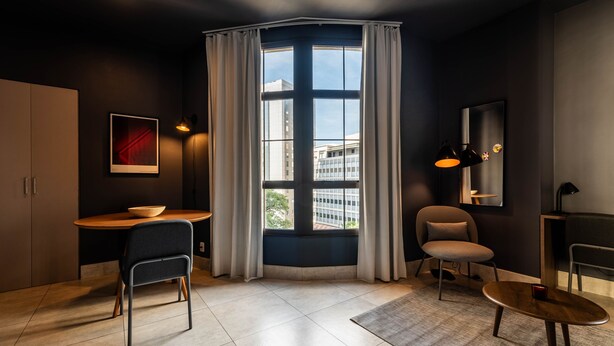 A modern room with a large window, a desk, two chairs, and a small table. - Jp047 Jacques Pilon Residence 3 Pessoas (São Paulo)