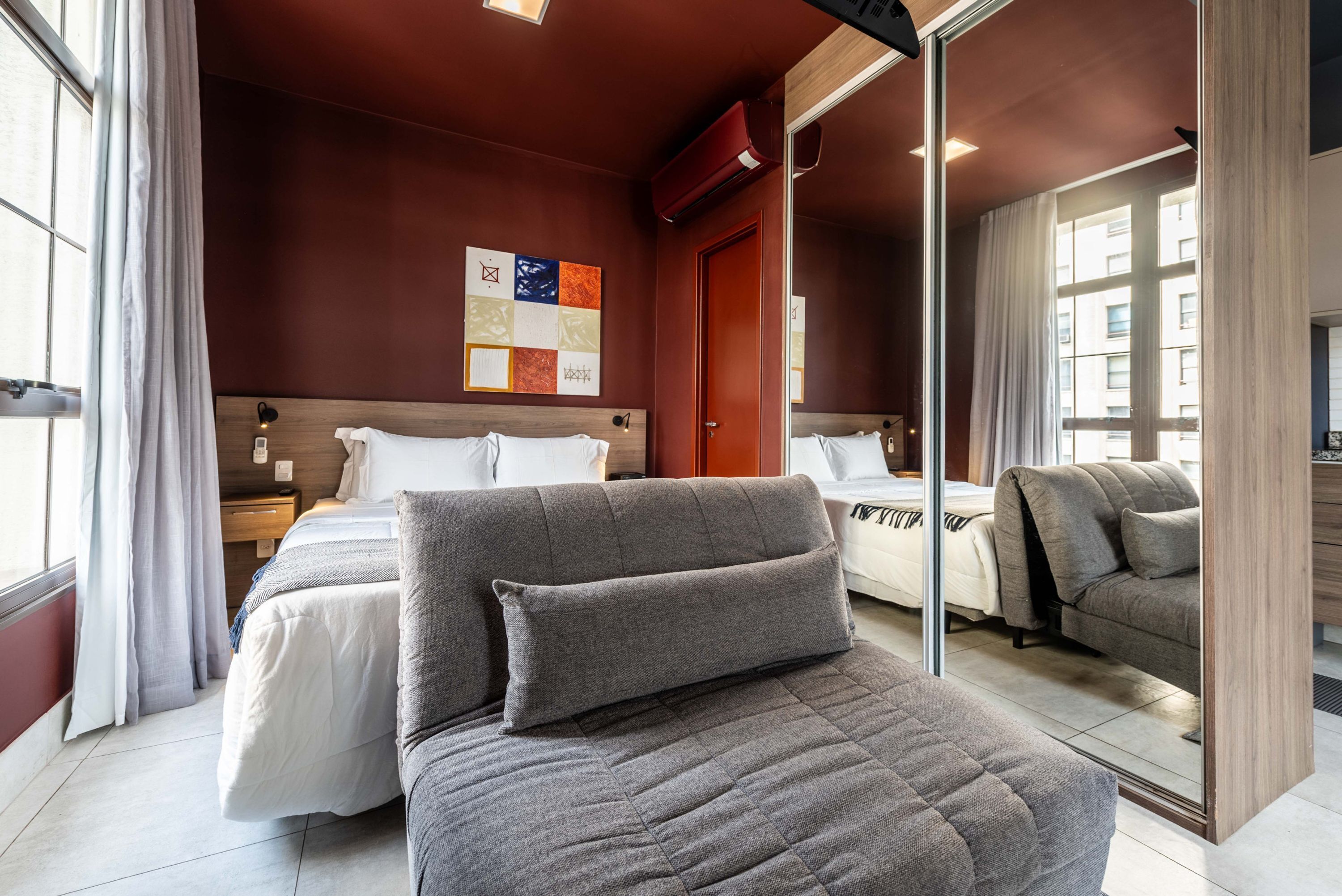 A hotel room with a large bed, a sofa, a desk, and a mirror.