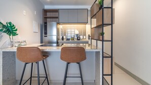 A modern kitchen with a central island, two bar stools, a built-in refrigerator, and a wooden shelving unit. - Landing 508 in S o Paulo (São Paulo)