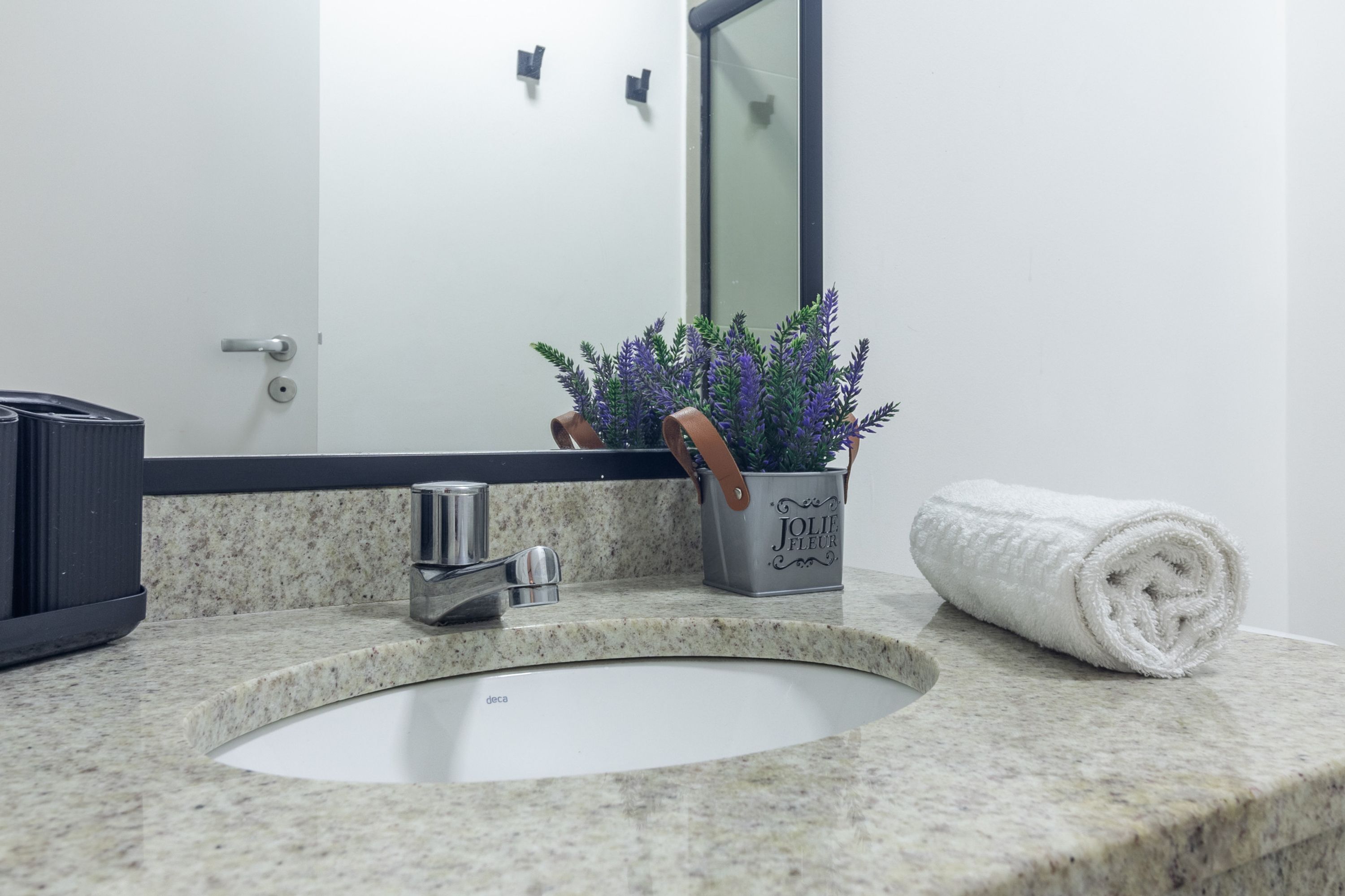 A bathroom with a granite countertop, a white sink, a mirror, a towel, and a potted plant.