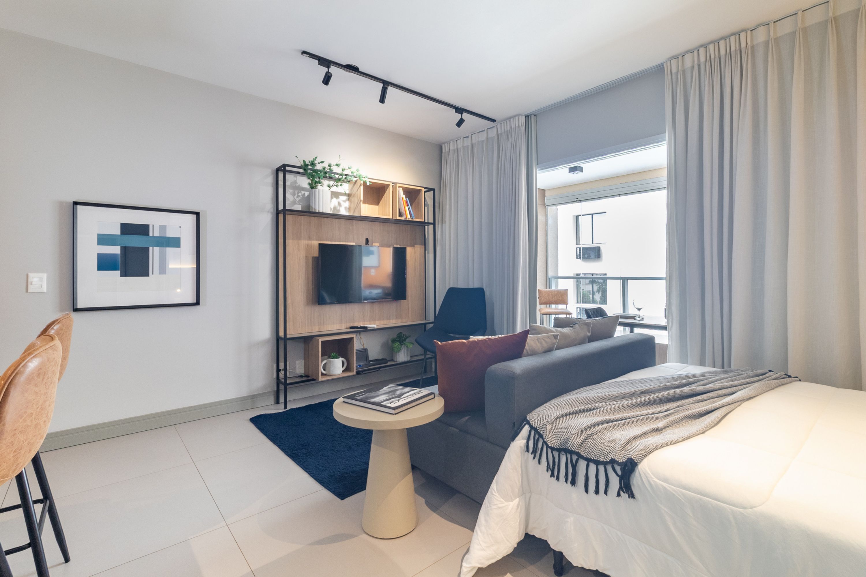 A modern hotel room with a bed, sofa, TV, and a small table.