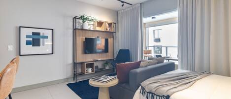 A modern hotel room with a bed, sofa, TV, and a small table.