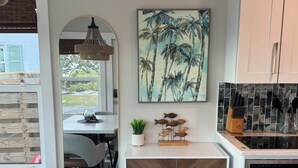 Una cocina moderna con comedor, que incluye un armario de madera, un cuadro de palmeras y un salpicadero de azulejos.