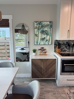 A modern kitchen with a dining area, featuring a wooden cabinet, a painting of palm trees, and a tiled backsplash. - Stunning Lemon Bay Water & Sunset Facing Home!  Water view from every window! (Englewood)