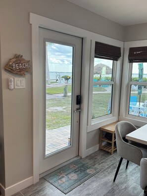 A room with a view of the beach, a door, a bench, and a table.