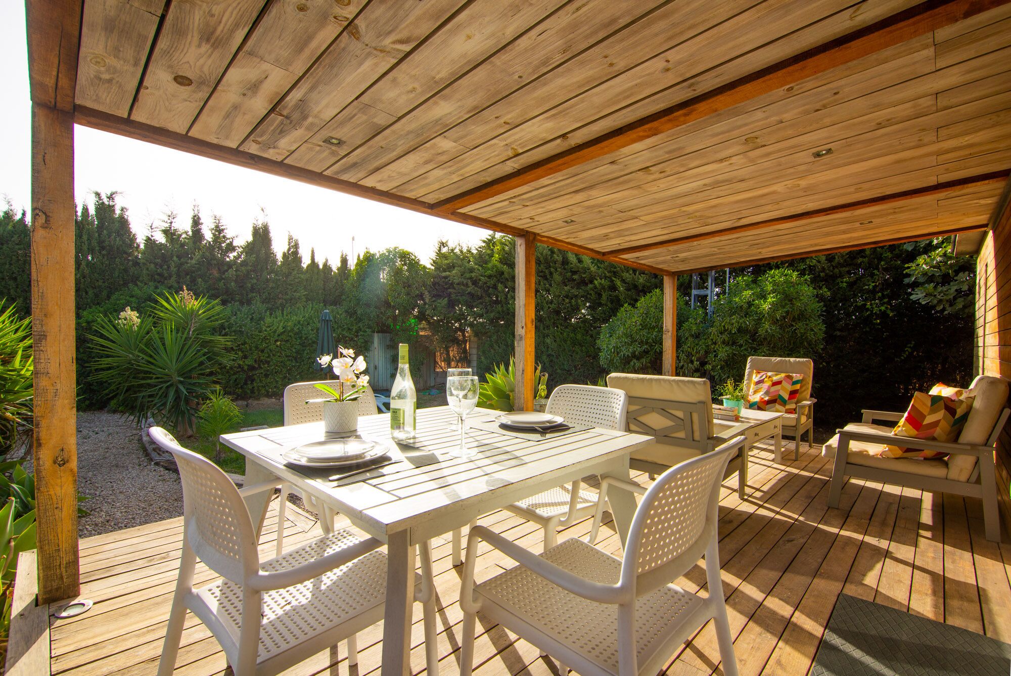 A covered outdoor patio with a table set for dining, surrounded by chairs.