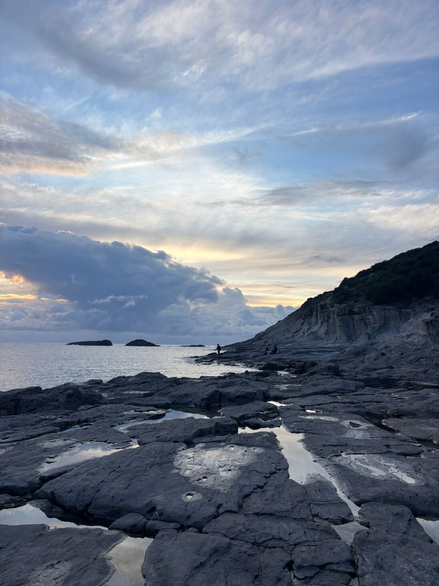 A rocky shoreline with calm water, a distant island, and a cliff.