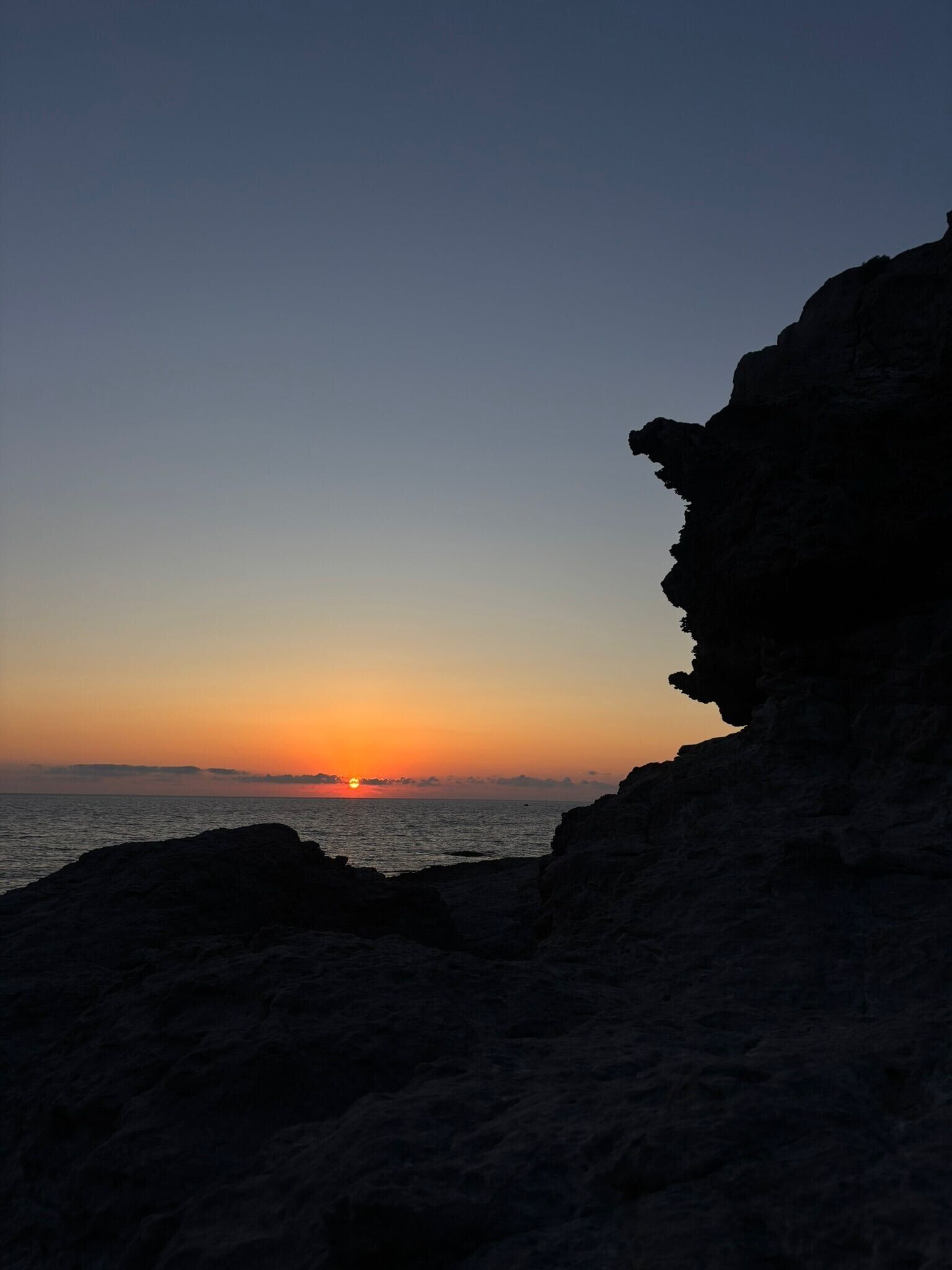 Een kustzonsondergang met een rotsachtige klif op de voorgrond.