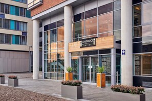 A modern hotel exterior with Staybridge Suites branding, large windows, and potted plants.