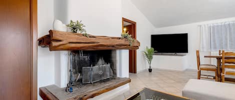 A living room with a fireplace, a television mounted on the wall, and a seating area with a sofa and a chair.