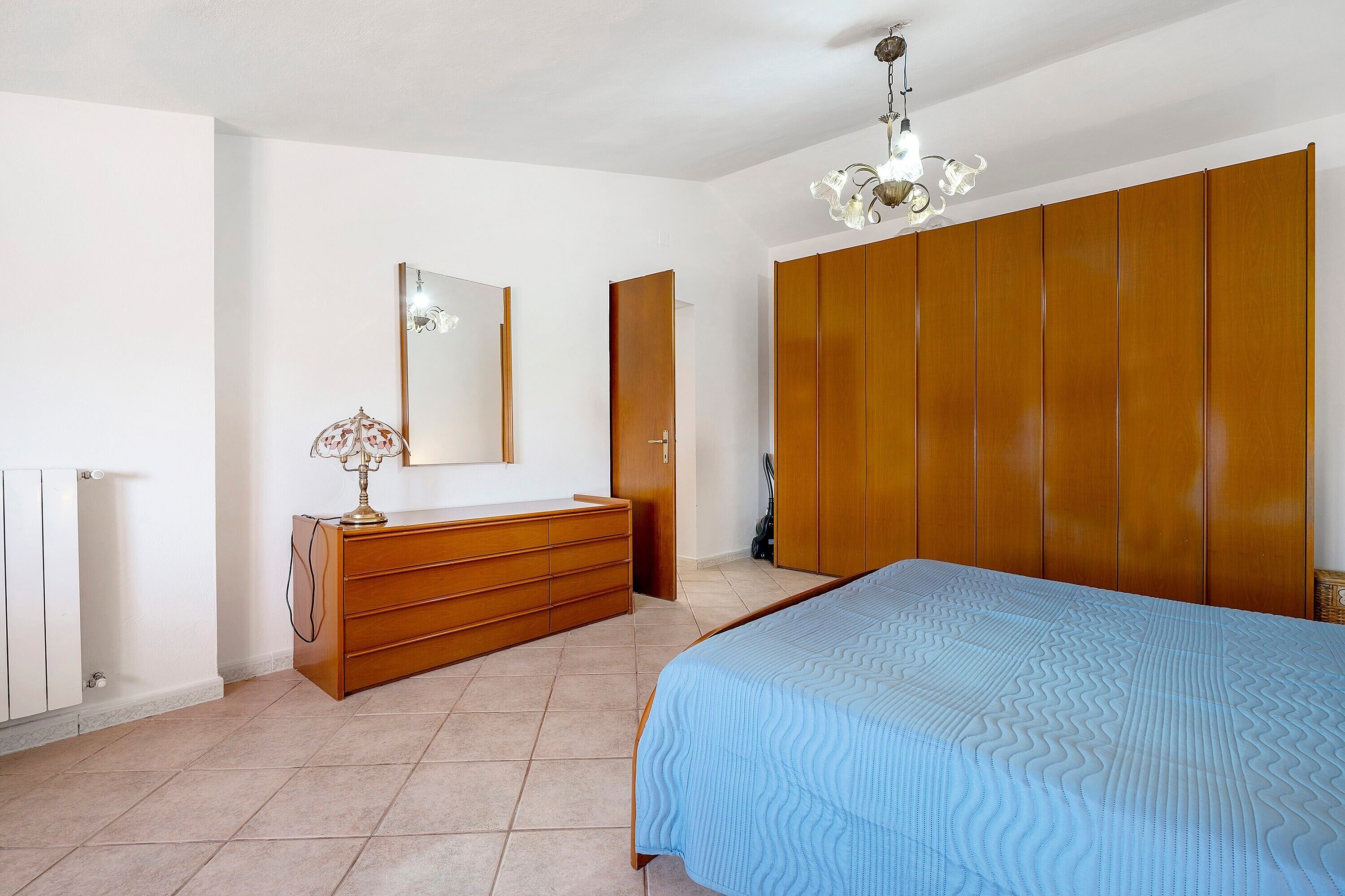 Ein Schlafzimmer mit Bett, Schminktisch, Spiegel, Kleiderschrank und einer Kandelaber.