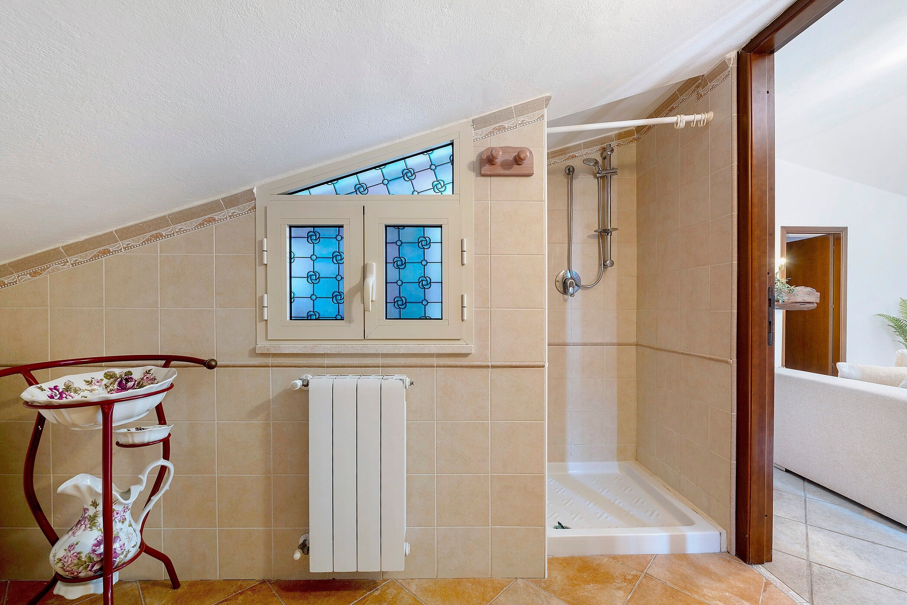 Un bagno con doccia, un termosifone e una finestra con vetrate colorate.