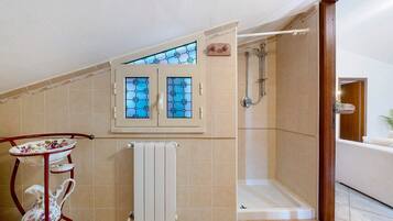 Un bagno con doccia, un termosifone e una finestra con vetrate colorate.