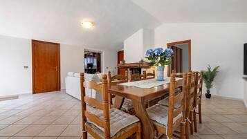 Un coin repas avec une table et des chaises en bois, un vase rempli de fleurs et une vue sur la cuisine.