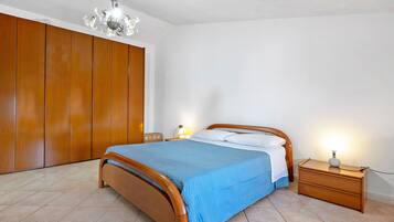 Ein Schlafzimmer mit einem hölzernen Bett, einem Nachttisch mit Lampe, einem Kleiderschrank und einer Pendelleuchte.