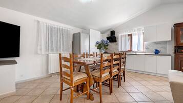 Eine moderne Küche mit weißen Schränken, einem Esstisch mit Holzstühlen und einem an der Wand befestigten Fernseher.