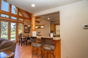 A spacious kitchen with wooden beams, a bar area with stools, and large windows offering a view of the outdoors.