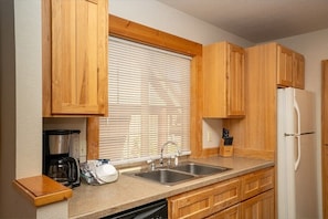 A kitchen with wooden cabinets, a double sink, a coffee maker, and a refrigerator.
