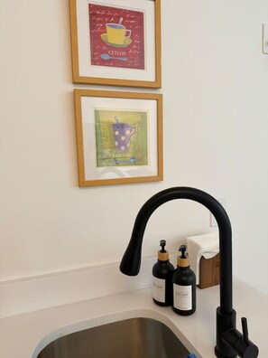 A kitchen with a modern faucet, two bottles of soap, and two framed pictures on the wall. - Luxury Studio Near Yale | Gym, W/D & Fast WiFi (New Haven)