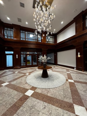 A spacious lobby with a large chandelier, a central round table with a vase, and a checkered floor.