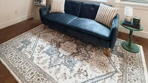 A living room with a dark blue sofa, patterned rug, and a television mounted on the wall.