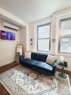 A living room with a dark blue sofa, patterned rug, and a television mounted on the wall.