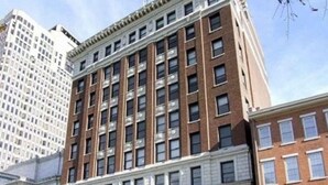 A multi-story building with a classical architectural style, featuring a central entrance with green awnings, large windows, and a brick facade.