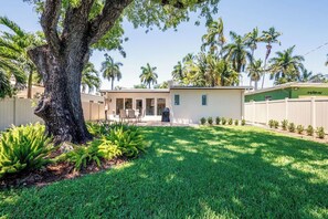 Propiedad residencial con un gran árbol, césped bien cuidado y una casa con patio y garaje.