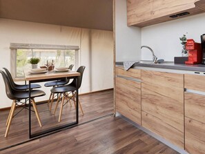 Een compacte keuken met houten kastjes, een eettafel met stoelen, een raam met uitzicht en een wastafel met kraan.