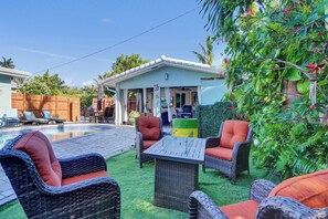 Ein Poolbereich mit Korbmöbeln, einer überdachten Terrasse und üppiger Bepflanzung.