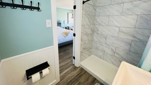 Et badeværelse med bruser, håndklædetørre og toiletpapirholder.